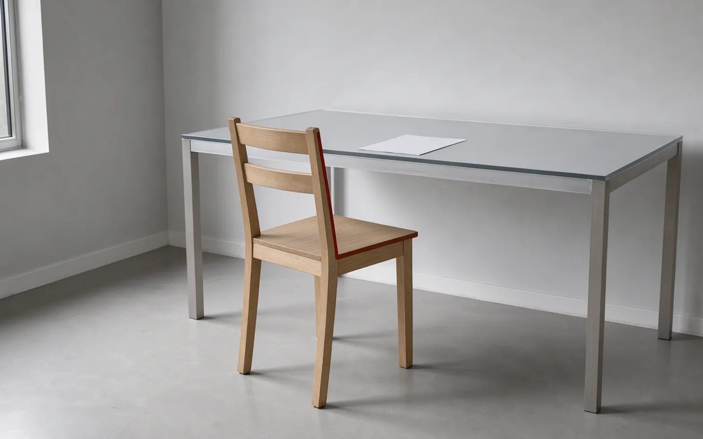 One empty chair drawn up to a clear writing table in soft daylight.
