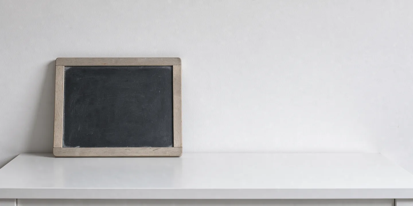 An unmarked chalk slate leaning against a plain white wall.